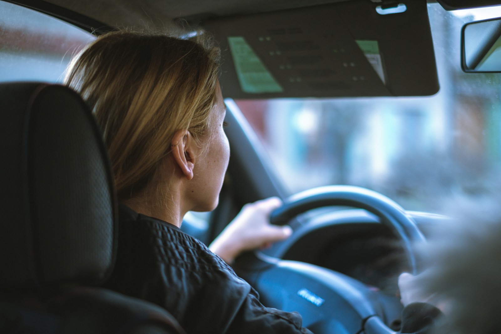 a woman sitting in a car with a steering wheel, auto